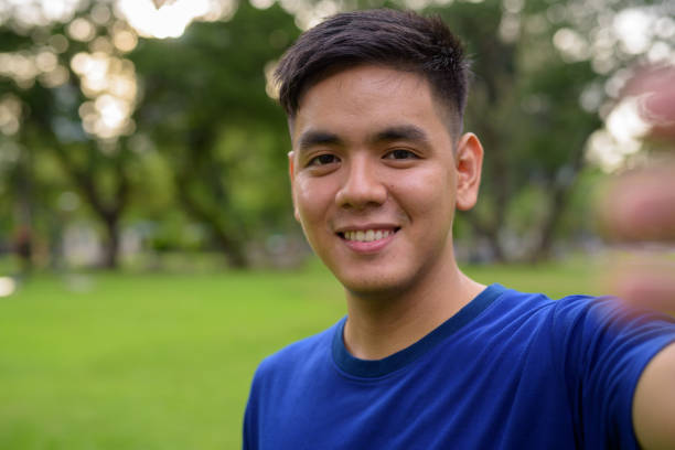 Portrait of young handsome Asian man relaxing at the park in Bangkok Thailand horizontal shot
